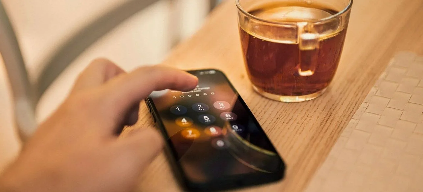 main tenant un smartphone à côté d'une tasse de thé sur une table en bois, symbolisant la gestion des réseaux sociaux au quotidien